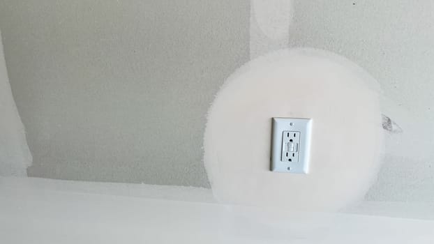 Castle Pines, Colorado USA - January 18, 2023-A GFCI outlet installed on a partially finished garage wall in a new single-family home under construction. The drywall shows a sanded area around the outlet, indicating ongoing preparation for painting or finishing.