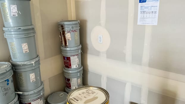Castle Pines, Colorado USA - January 18, 2023-Stacked paint buckets and supplies in the garage of a single-family home under construction. The unfinished drywall features a GFCI outlet and taped seams, indicating ongoing preparation for interior finishing. A construction notice is posted on the wall.