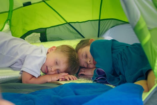 An adorable and heartwarming scene of two young kids peacefully sleeping inside a vibrant and colorful camping tent