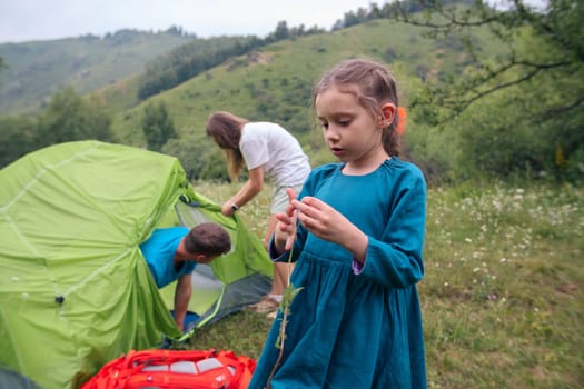 A cheerful family sets up a tent while a child explores nature, capturing the essence of outdoor adventure