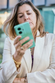 Smiling middle-aged businesswoman using a smartphone outdoors in a modern urban setting.