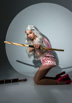 blonde girl holding bow and arrow on valentine's day. She has a big wooden bow in her hands. The girl is beautiful with bright makeup. She is wearing pink shoes. photo taken in studio