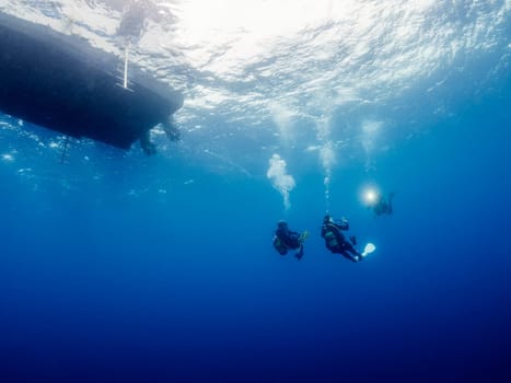 scuba divers in wetsuit taking picture while diving making the safety stop near of the boat before rising to the surface, concept of active leisure and underwater adventure, copyspace for text