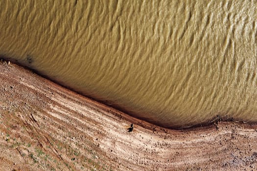 drone view of river with rippled water surface flowing near stony shore with dried surface in nature, concept of environment and ecology