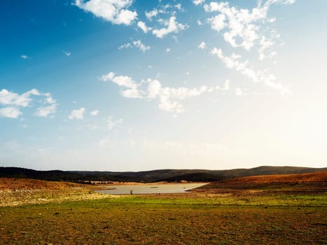 large open field with a lake in the middle, the sky is clear and blue with few clouds scattered, concept of peaceful and serene landscape in the vast expanse of land, copyspace for text