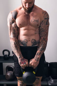 powerful shirtless bodybuilder with tattoos doing exercise with heavy kettlebell during functional training in gym, concept of fitness and active lifestyle