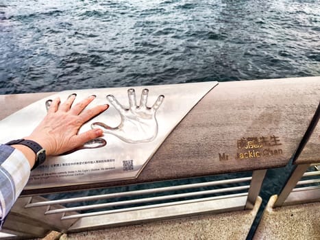 Hong Kong - April 05, 2024: An individual places their hand over the handprint of Jackie Chan at the waterfront in Hong Kong, surrounded by a serene atmosphere ideal for stargazing at night.