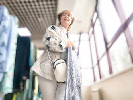 A middle aged woman stands happily in a store, holding shopping items while exploring various products around her in a vibrant space.