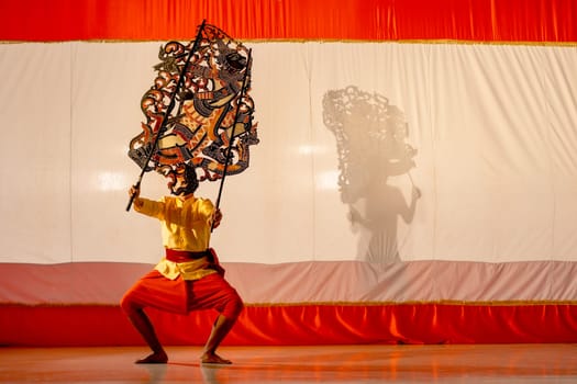Asian young man stand with perform grand shadow play in front of his team stay behide in the shadow of other charactor craft.