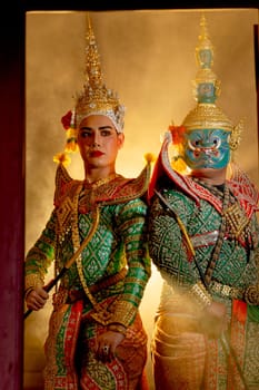 Vertical image two charactors of Khon mask costume stand with backs leaning against each other and giant mask stand in right side at door frame with beam light in the back.