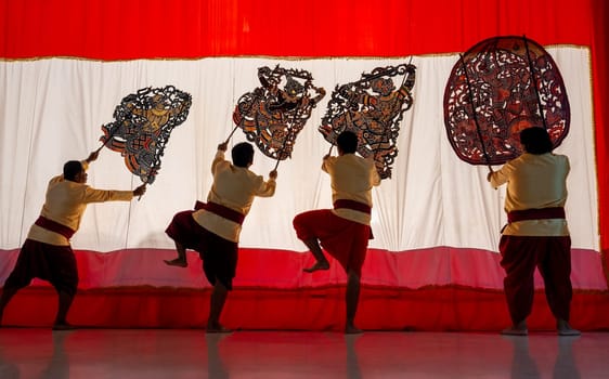 Four player men stand with perform grand shadow play in front of white screen with some of them lift leg as performance of the show.