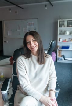 elegant woman over 40, business lady, works in the office. she is well-groomed, dressed in a white sweater. she smiles