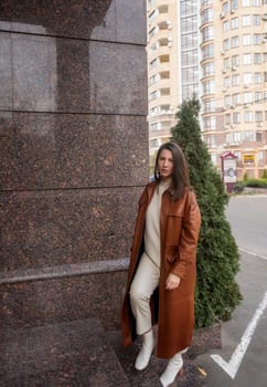 elegant woman over 40 exiting building with laptop bag. She is wearing a brown coat, holding a laptop bag. She is elegant in white shoes. She is a slim, well-groomed woman working in an office.