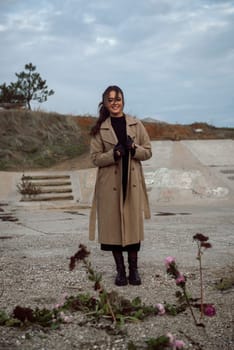 young girl on the seashore around the rocks. she is dressed in a beige trench coat, she is dreaming on the seashore among the flowers of the chrysanthemum variety. a chair decorated with blue fabric