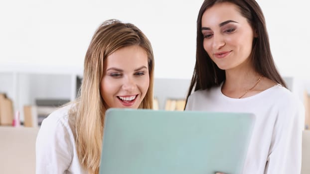 Two pretty women watching a funny video on a laptop laugh and smiling