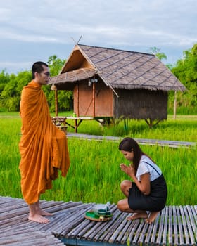 Suphanburi Thailand 22 September 2023, a Thai woman giving food at a monk in the morning surrounded by green rice paddy fields