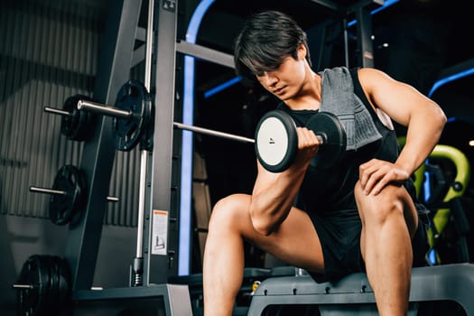 A young man sitting on an exercise bench holding a heavy dumbbell, working on his arm muscles and bicep, with great concentration and determination. empty space