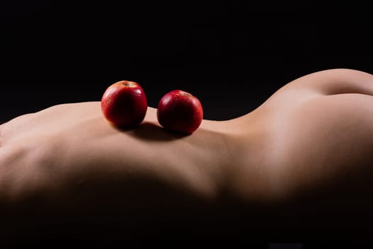 Nude woman with a red apple on her back, dark background