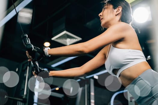 Beautiful woman working out indoors, using a pull-down weight machine to train her arms and build muscle. fitness center health workout concept