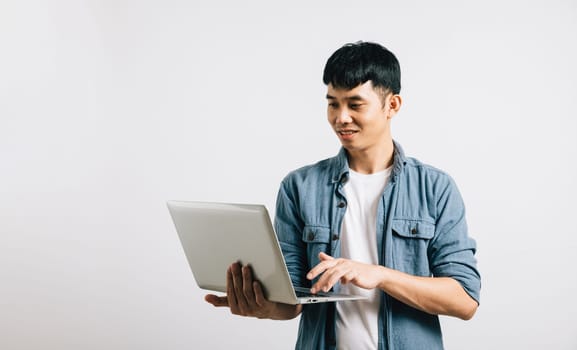 Excited and happy young Asian man smiles with confidence, using laptop to send emails or chat on a social network. Studio shot isolated on white, pretty face reflects the joy of online communication.