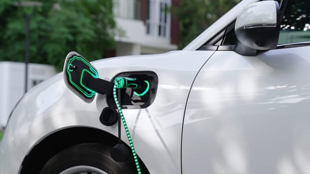 Electric car plugged in with home charging station to recharge battery by EV charger cable. Future innovative EV car and energy sustainability. Smart and futuristic home energy infrastructure. Peruse