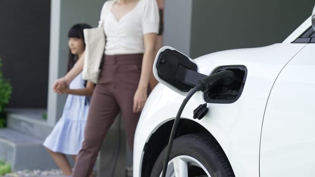 Progressive lifestyle of mother and daughter who have just returned from school in an electric vehicle that is being charged at home. Electric vehicle powered by sustainable clean energy.