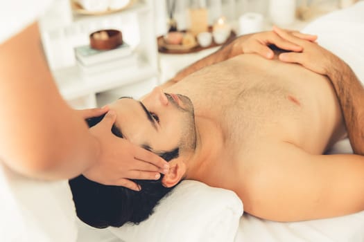 Caucasian man enjoying relaxing anti-stress head massage and pampering facial beauty skin recreation leisure in dayspa modern light ambient at luxury resort or hotel spa salon. Quiescent