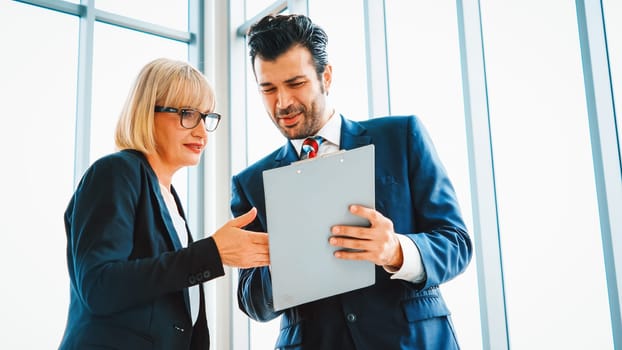 Two business people talk project strategy at office meeting room. Businessman discuss project planning with colleague at modern workplace while having conversation and advice on financial report. Jivy