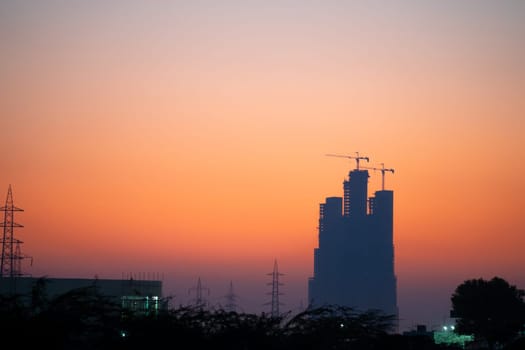 Evening dusk twilight shot showing under construction skyscraper multi story building silhouette against golden, red sky in Indian cities