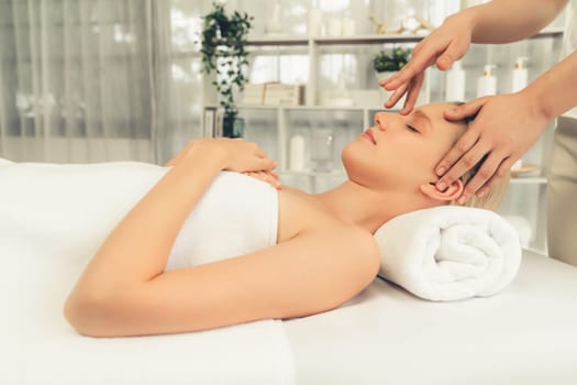 Caucasian woman enjoying relaxing anti-stress head massage and pampering facial beauty skin recreation leisure in dayspa modern light ambient at luxury resort or hotel spa salon. Quiescent