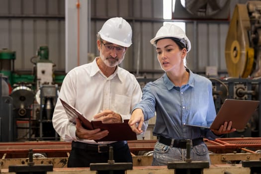 Factory engineer manager with assistant using laptop to conduct inspection of steel industrial machine, exemplifying leadership as machinery engineering inspection supervisor in metalwork manufacture.