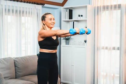 Athletic and sporty senior woman engaging in body workout routine with lifting dumbbell at home as concept of healthy fit body with body weight lifestyle after retirement. Clout