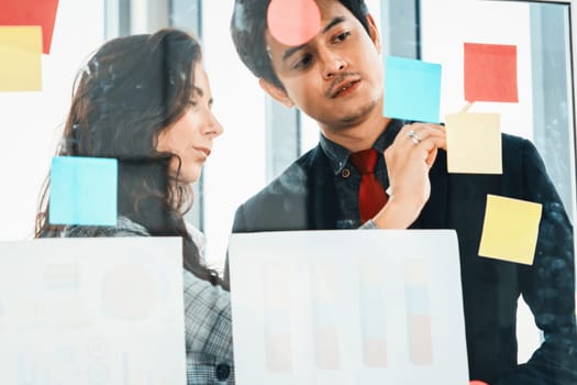 Business people work on project planning board in office and having conversation with coworker friend to analyze project development . They use sticky notes posted on glass to make it organized. Jivy