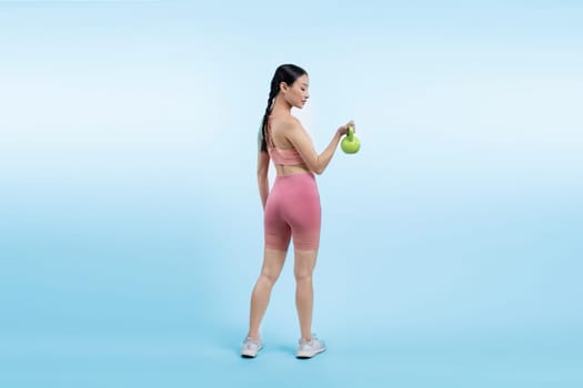 Vigorous energetic woman doing kettlebell weight lifting exercise on isolated background. Young athletic asian woman strength and endurance training session as body workout routine.