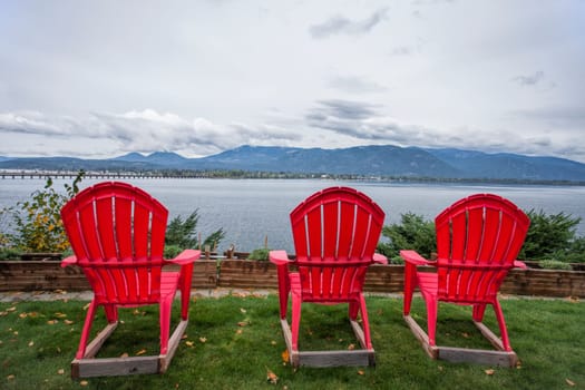 Three red lawn chairs sit in the yard overlooking the lake by Sandpoint, Idaho.