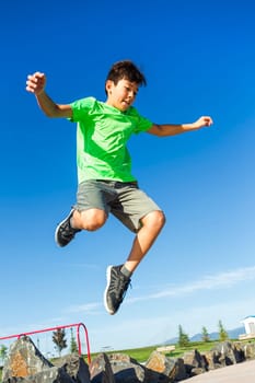 A young boy leaps off a rock in a park on a bright summer day.