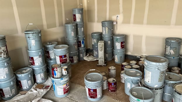 Castle Pines, Colorado USA - January 18, 2023-Garage interior of a new single-family home under construction, featuring numerous paint buckets stacked on the concrete floor. Unfinished drywall lines the walls, and the scene highlights the materials used during the home-building process.