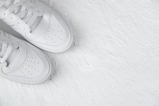 White leather sneakers stand in the left corner on a white textured background. High quality photo