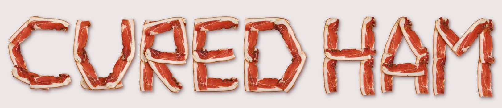 Cured ham is arranged in artistic letter shapes on a light background, showcasing vibrant colors and textures
