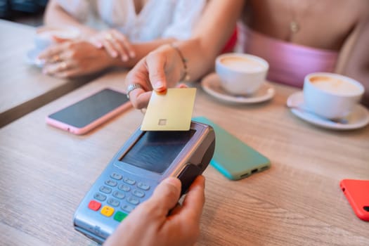 Close-up of a woman using a credit card for a contactless payment at a cafe. Coffee cups, smartphones, and a relaxed atmosphere in the background, symbolizing modern convenience.