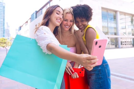 Three young women sitting outdoors, smiling, and taking a playful selfie together. Perfect for concepts like friendship, happiness, social media, and outdoor lifestyle.