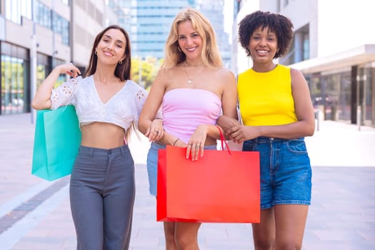 Three young women enjoying a sunny day, carrying shopping bags and smiling as they walk in an urban environment. Perfect for concepts like friendship, shopping, fashion, and lifestyle.