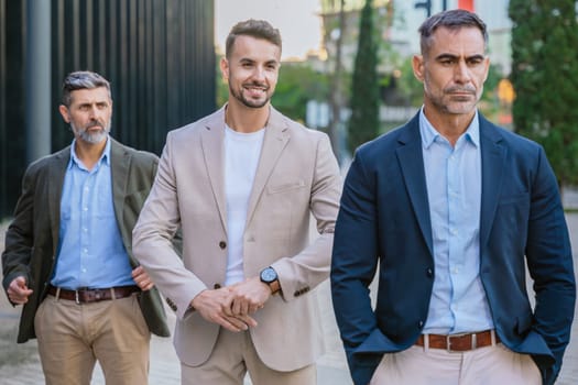 A group of three confident businessmen in formal and semi-formal attire walking outdoors. Modern urban setting highlights professionalism, leadership, and collaboration