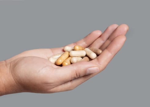 Cupped womans hand with a pile of mixed beige medical capsules closeup over grey background. Assorted pharmaceutical products for healthcare