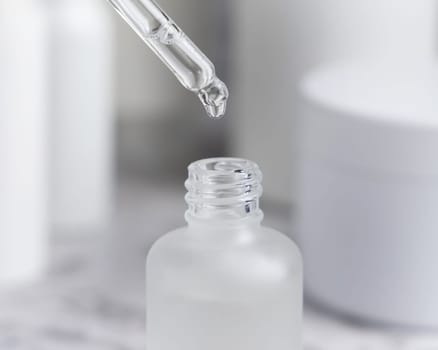 Drop falls from a pipette inside a trasparent glass dropper bottle against cosmetics in bathroom closeup. Natural organic serum or essence or for beauty routin, monochrome
