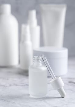 Pipette set near a trasparent glass dropper bottle on white marble near cosmetic bottles and jars in bathroom, close up, packaging mockup. Natural serum or essence