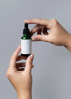 Female hand holding green dropper bottle with blank label against grey close up, cosmetic packaging mockup, copy space. Skincare beauty product - serum or essential oil