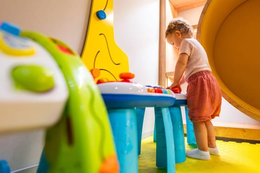 Toddler standing at colorful activity table in a bright indoor playroom with interactive toys