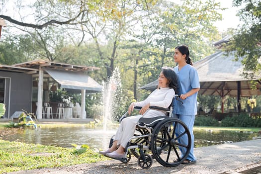 A nurse and elderly patient in a wheelchair admire the garden, enjoying a serene and sunny day outdoors.