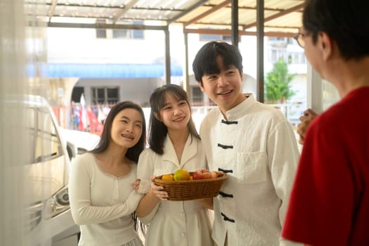 Cheerful family arriving at a relative home during Chinese New Year, carrying a basket of fruits as a gift.